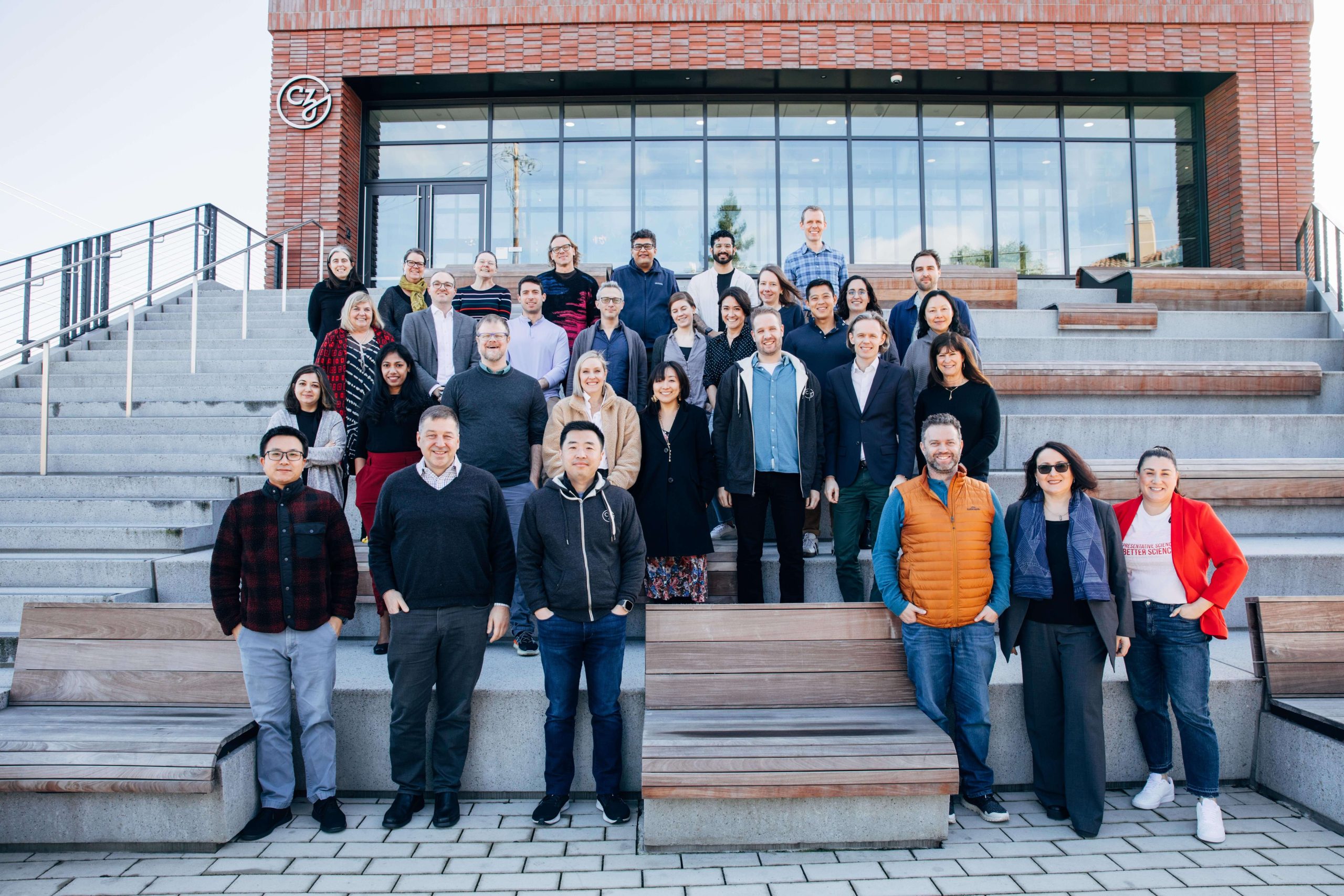 Participants of the Neuroscience Early Career Acceleration Retreat stand on the CZI headquarters steps to pose for a group picture on a cloudy morning.