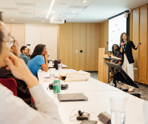 A woman stands at the front, delivering a presentation to a group of attentive listeners.