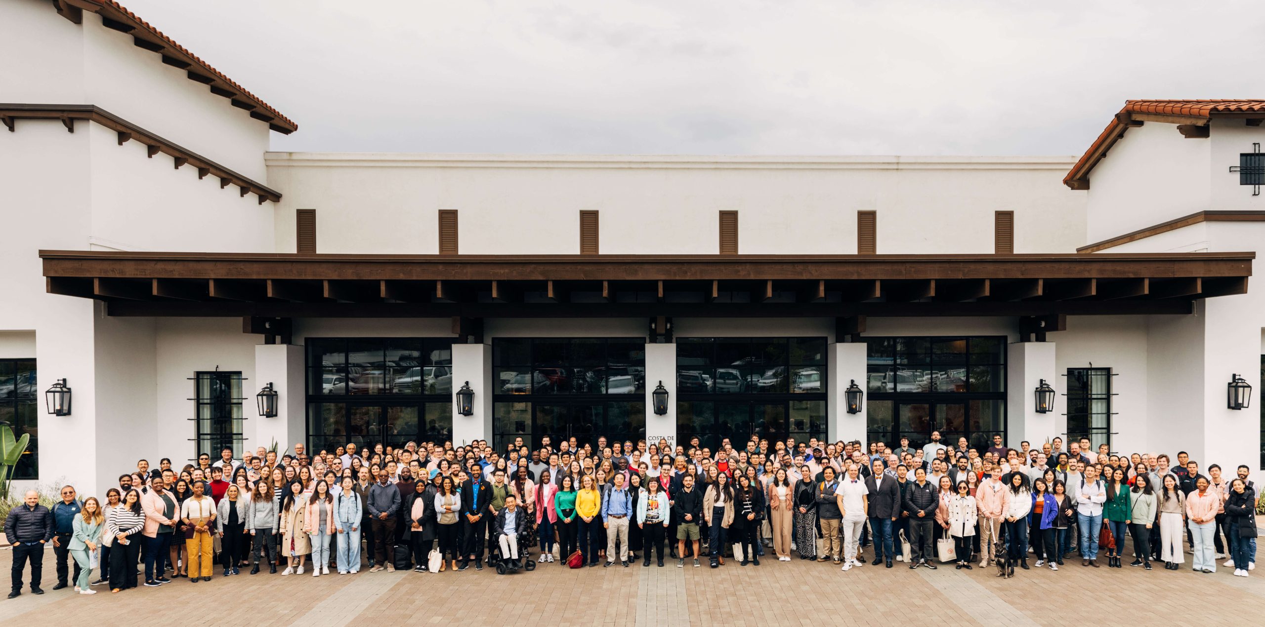 Single-Cell Biology 2023 Annual Meeting participants gather close together and smile at the camera. They stand in front of a white building.