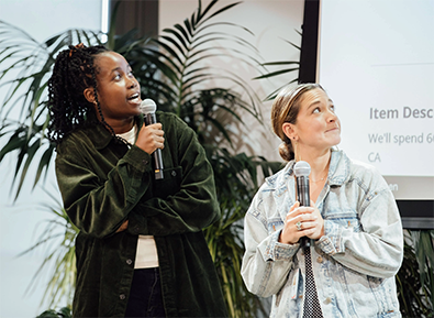 two women face an unseen audience at an event, both hold microphones