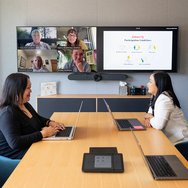 a group sits at a conference table during a virtual conference call