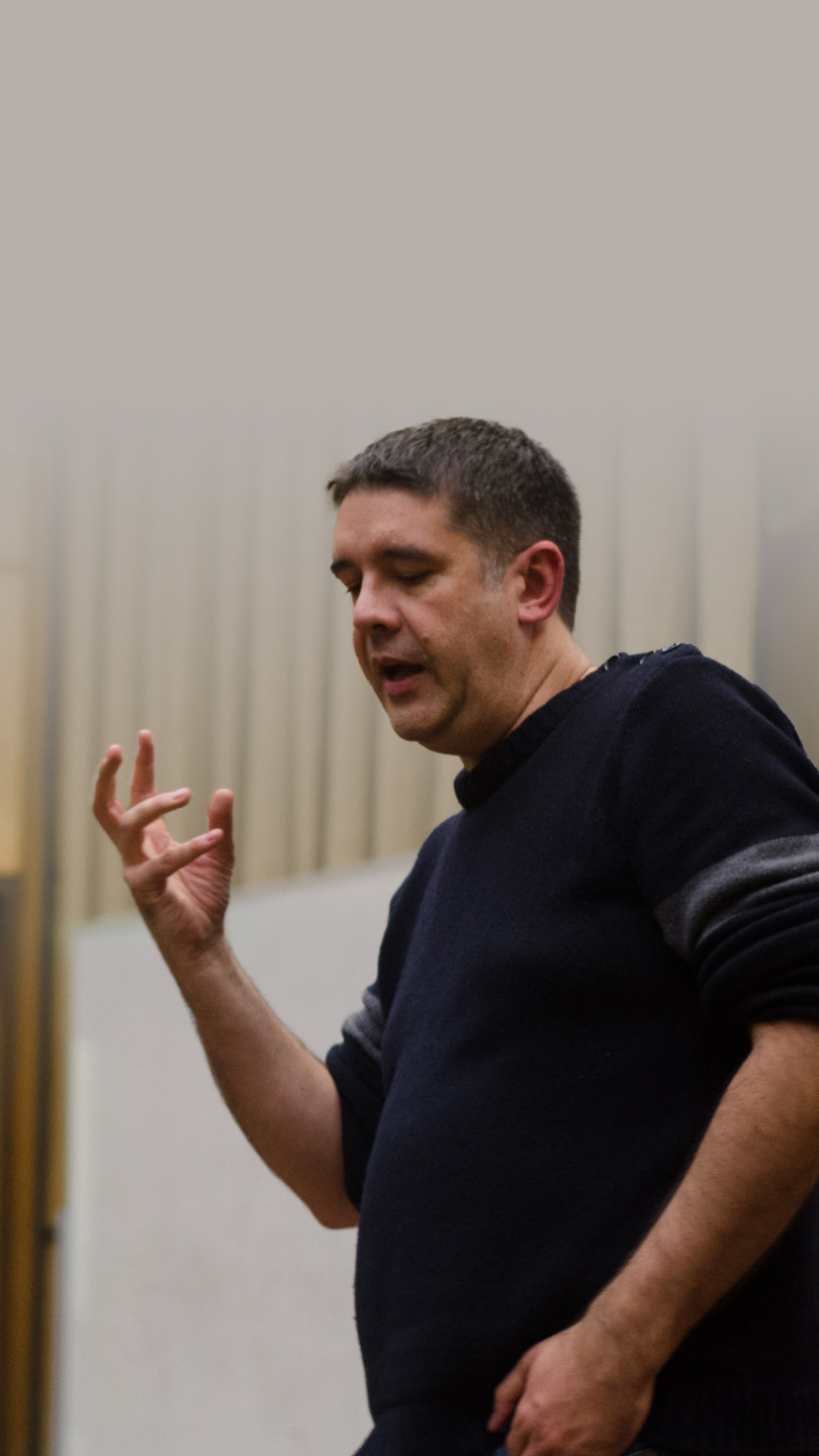 Dan Quine in a dark sweater and jeans gestures while speaking in a lecture hall.