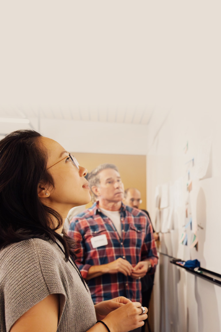 Sandra Liu Huang stands and looks up at a whiteboard with her hands in front of her.