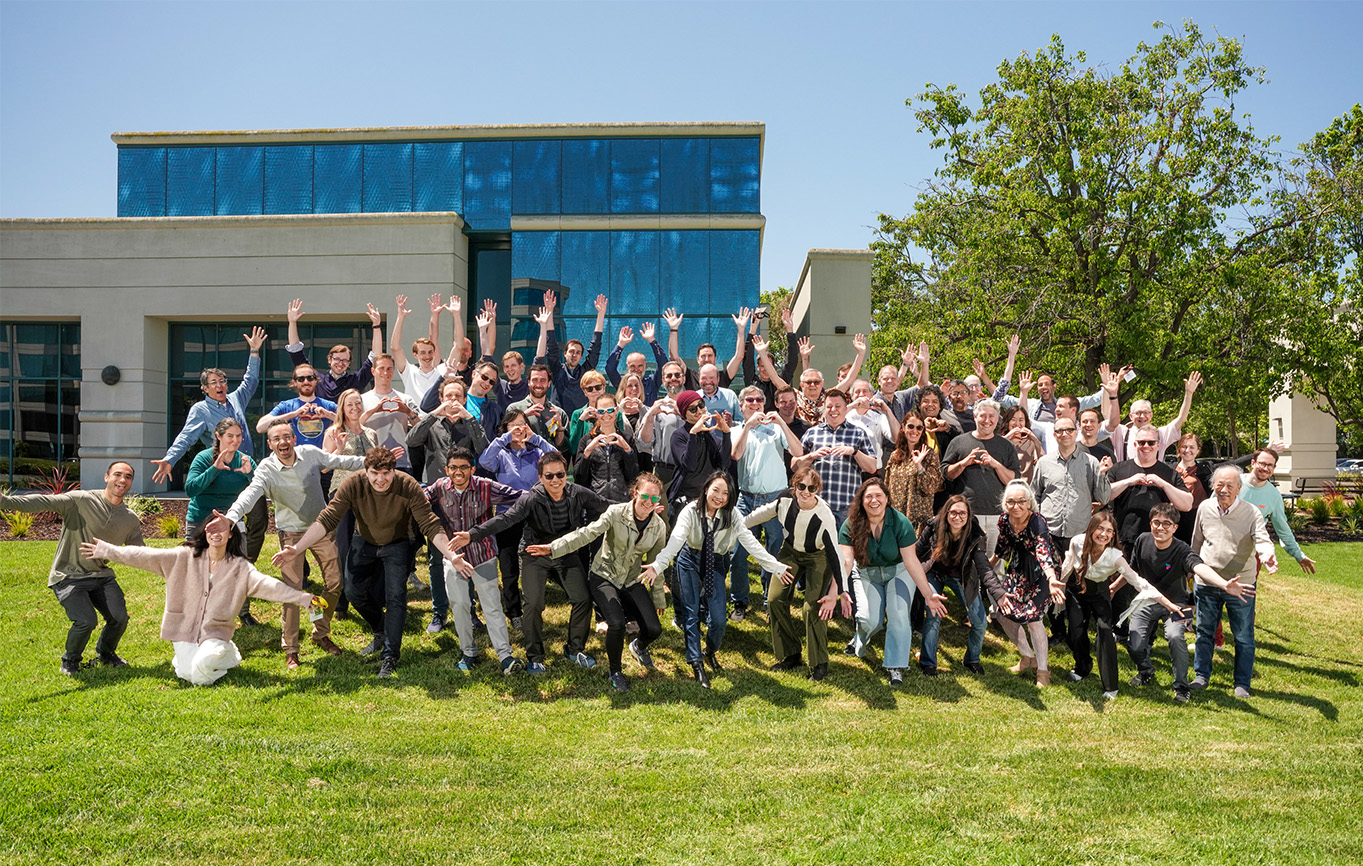Participants of the CZI Visual Proteomics Showcase making fun hand gestures on the lawn in front of the Sobrato Community Conference Center in Redwood City, CA.
