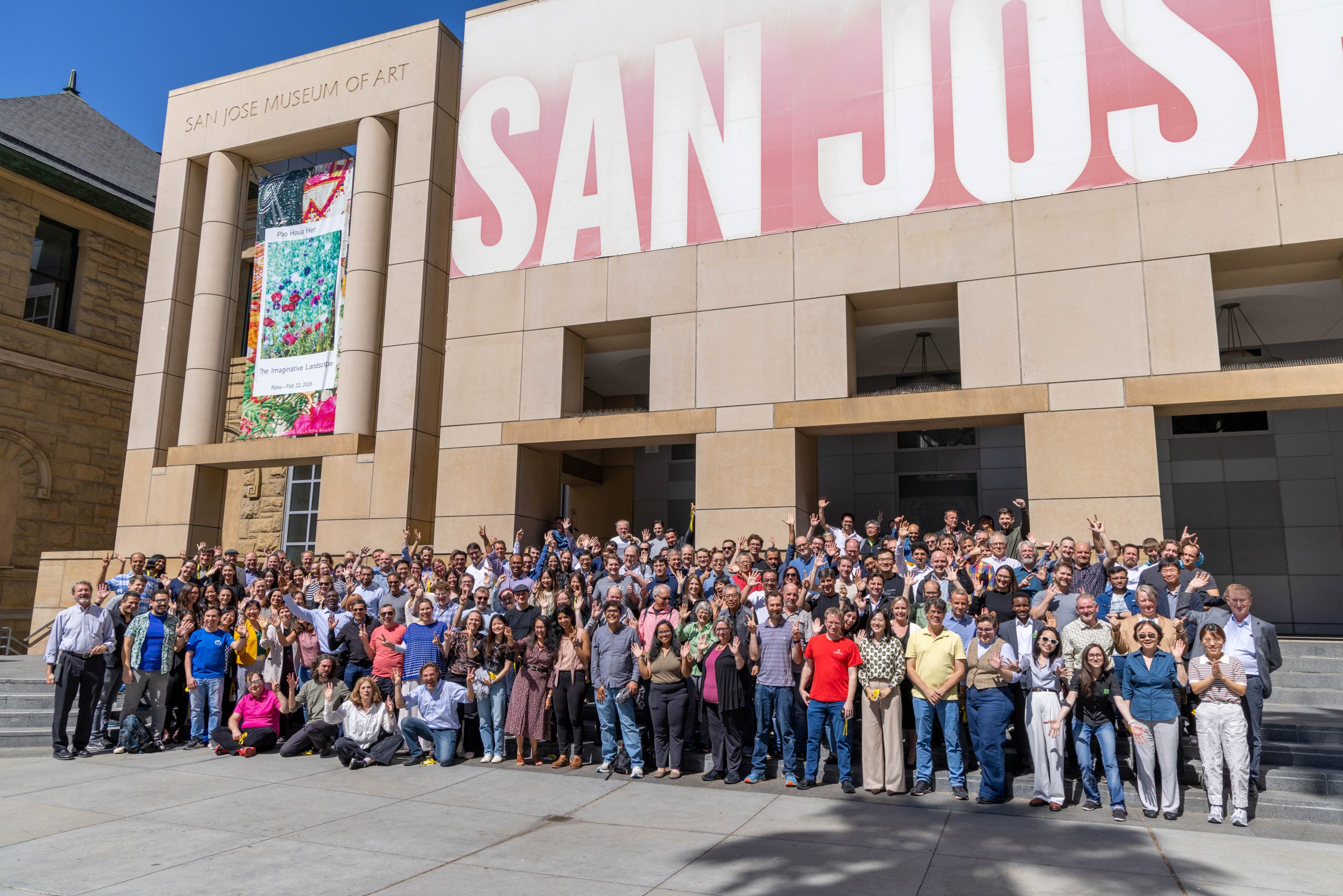 Participants of the CZI Imaging the Future 2025: Focusing on Biology in Action meeting smile and wave to the camera on the steps of the San Jose Museum of Art across from the Signia by Hilton San Jose in San Jose, CA.