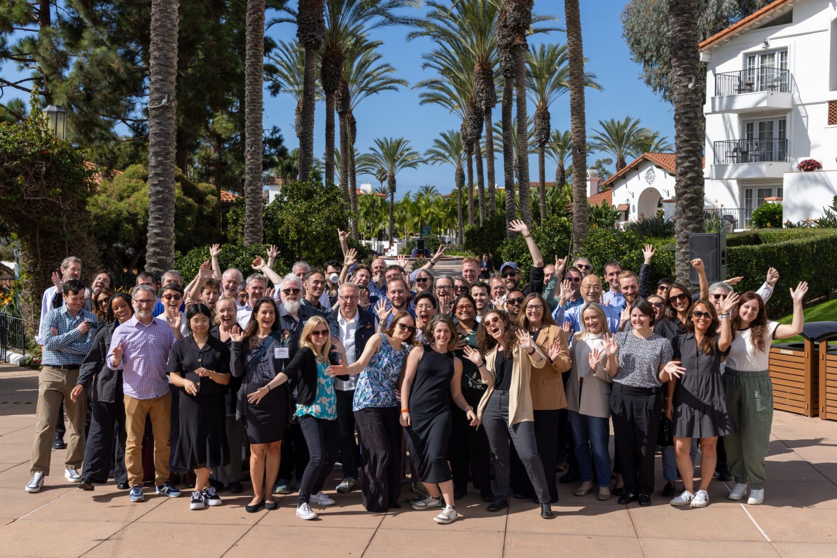 Participants of the openRxiv Meeting waving and smiling at the top of the steps of The Plaza courtyard at the Omni La Costa Resort & Spa in Carlsbad, CA.