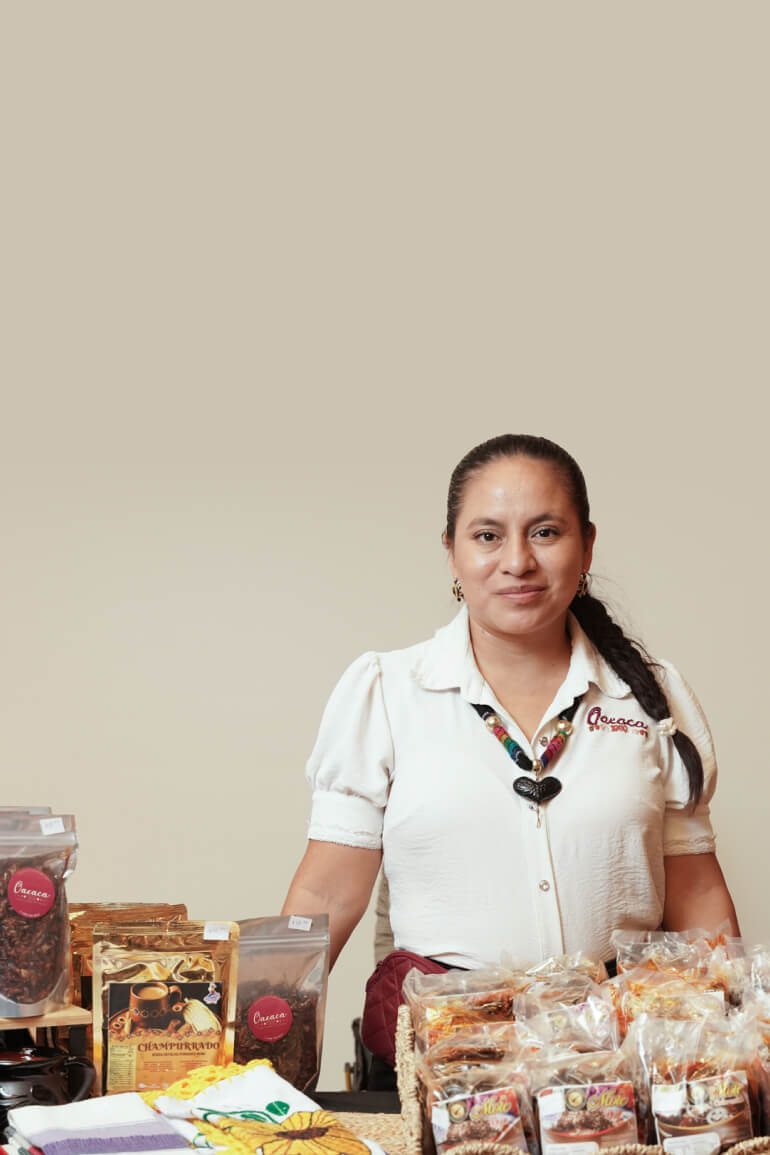 A smiling woman stands behind a table displaying goods.