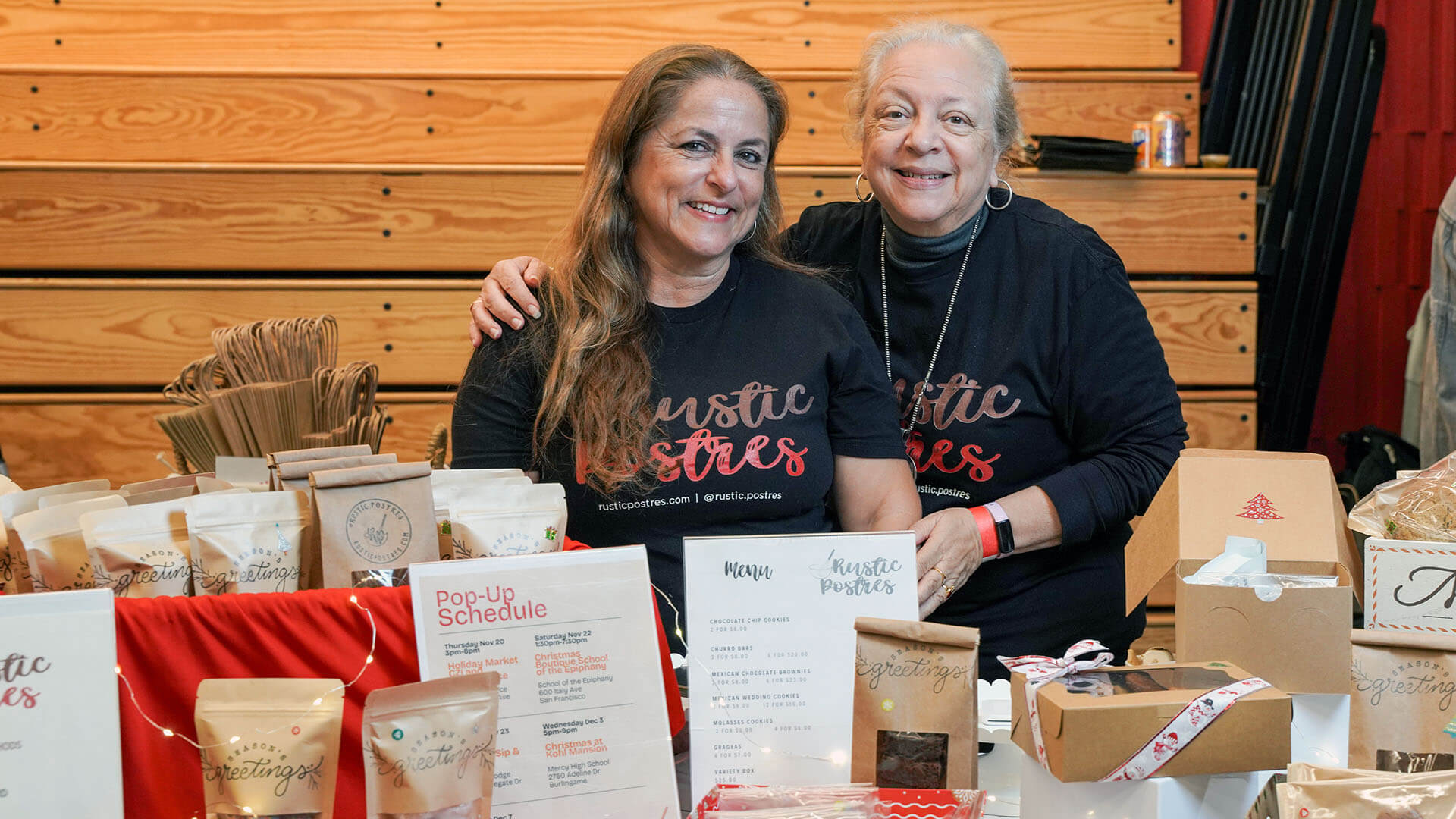 Two women pose and smile behind a display of holiday treats.