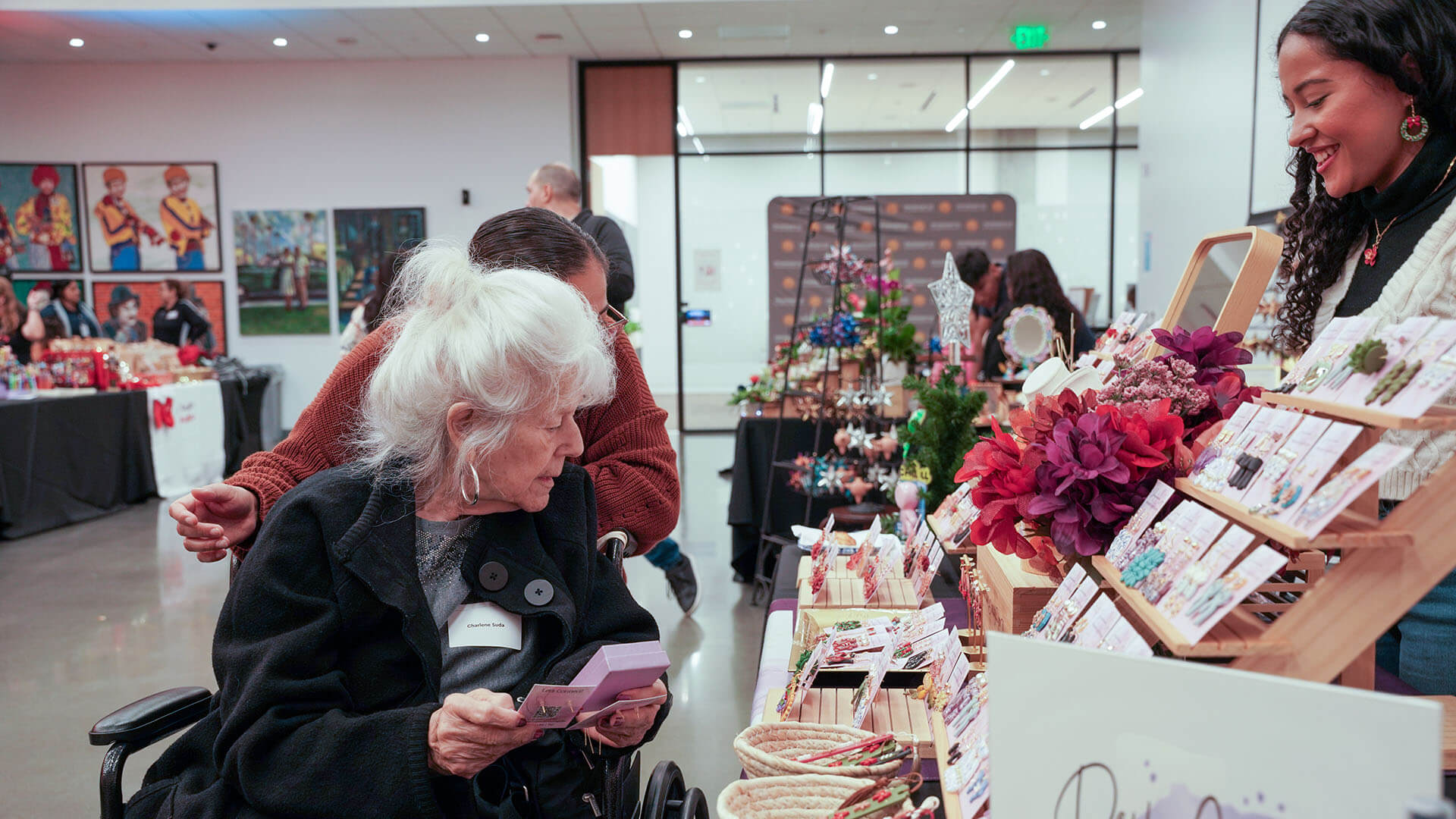 A woman shops for jewelry as the business owner stands behind a table display.