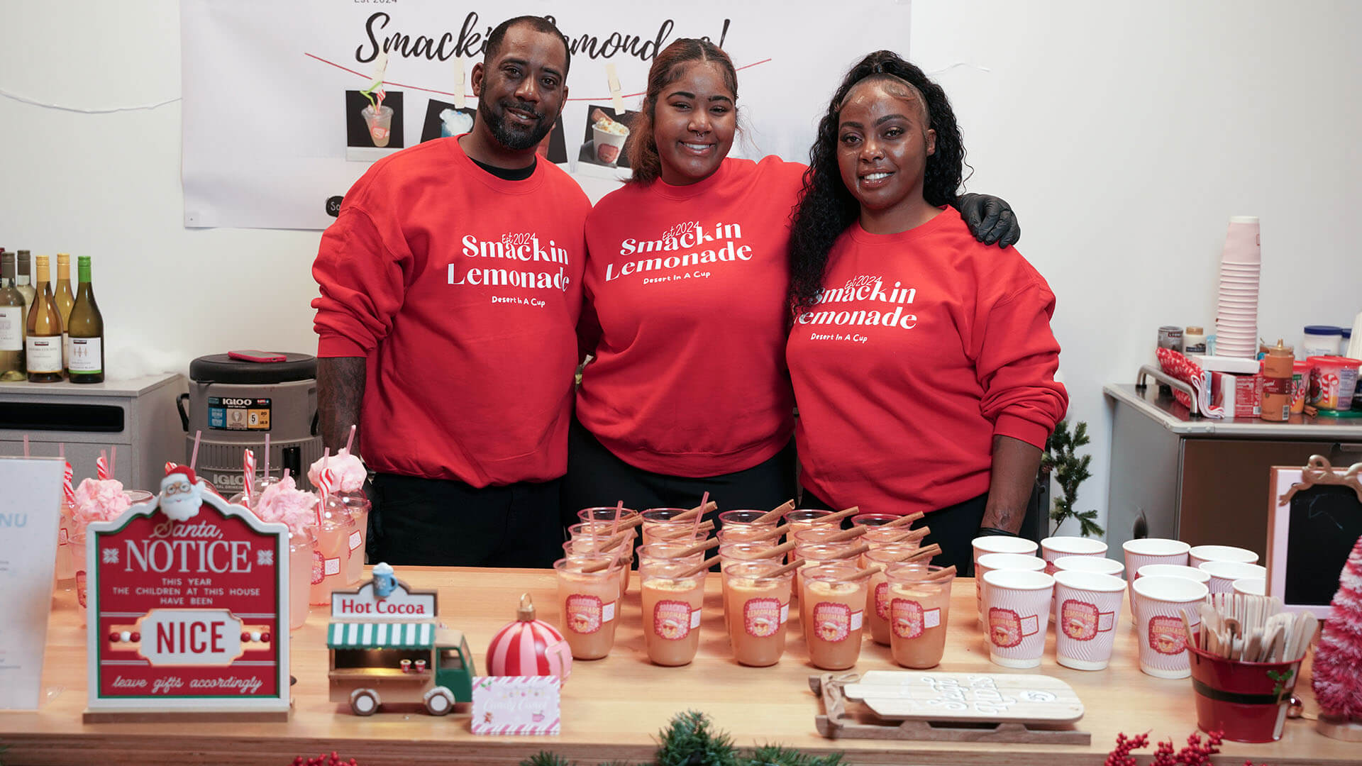 Three people pose in red sweatshirts behind a display of holiday drinks.