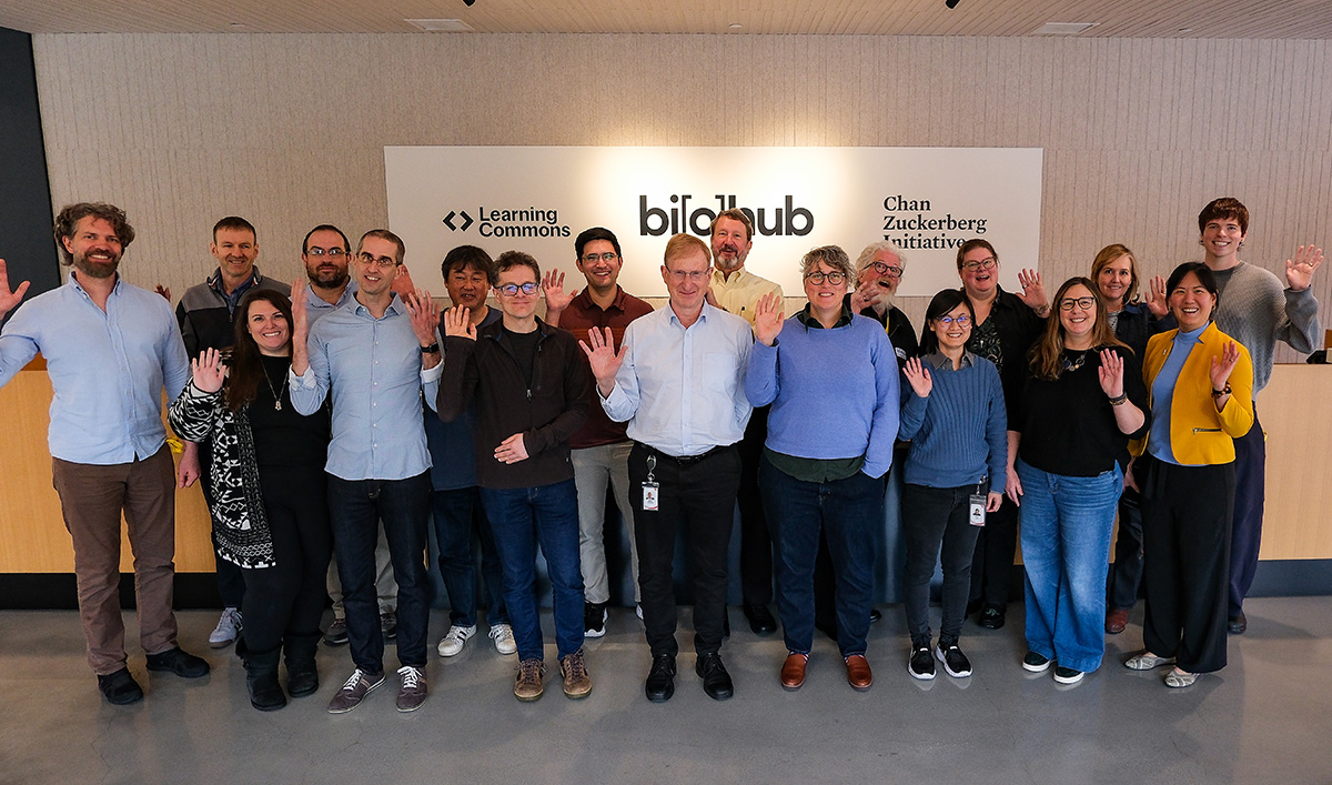 Group of workshop participants standing together and waving in front of a wall displaying Learning Commons, Biohub, and Chan Zuckerberg Initiative logos.