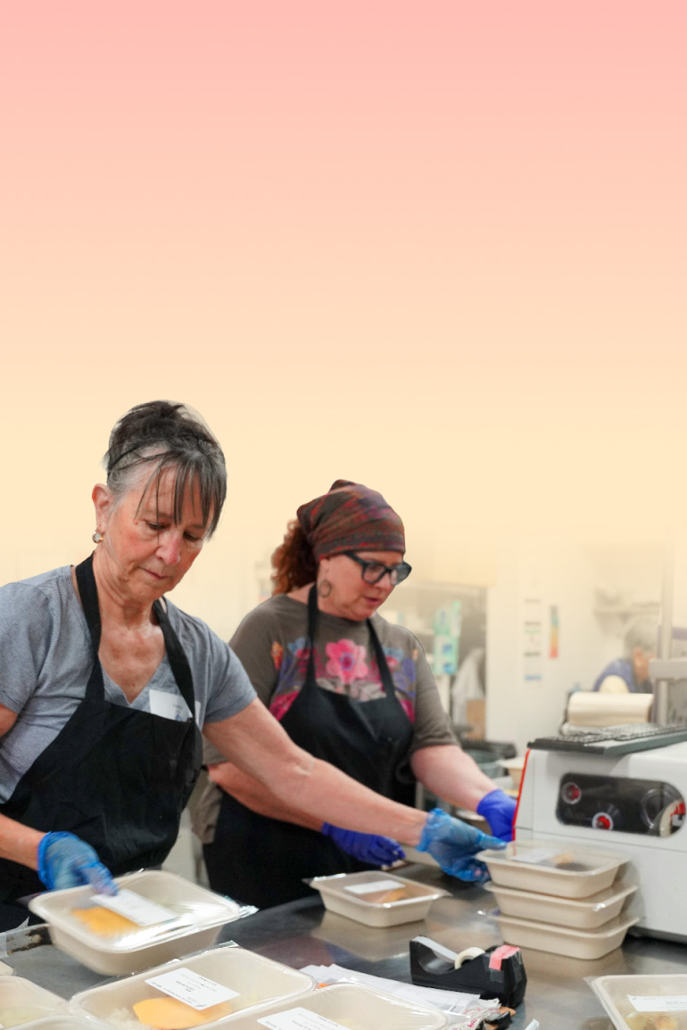 Volunteers preparing packaged meals in a commercial kitchen, representing the work of CZI's 2026 Community Fund grantees serving San Mateo County.