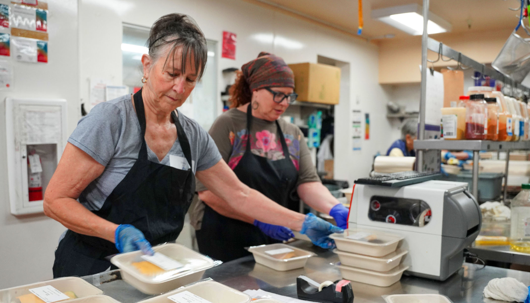 Volunteers preparing packaged meals in a commercial kitchen, representing the work of CZI's 2026 Community Fund grantees serving San Mateo County.