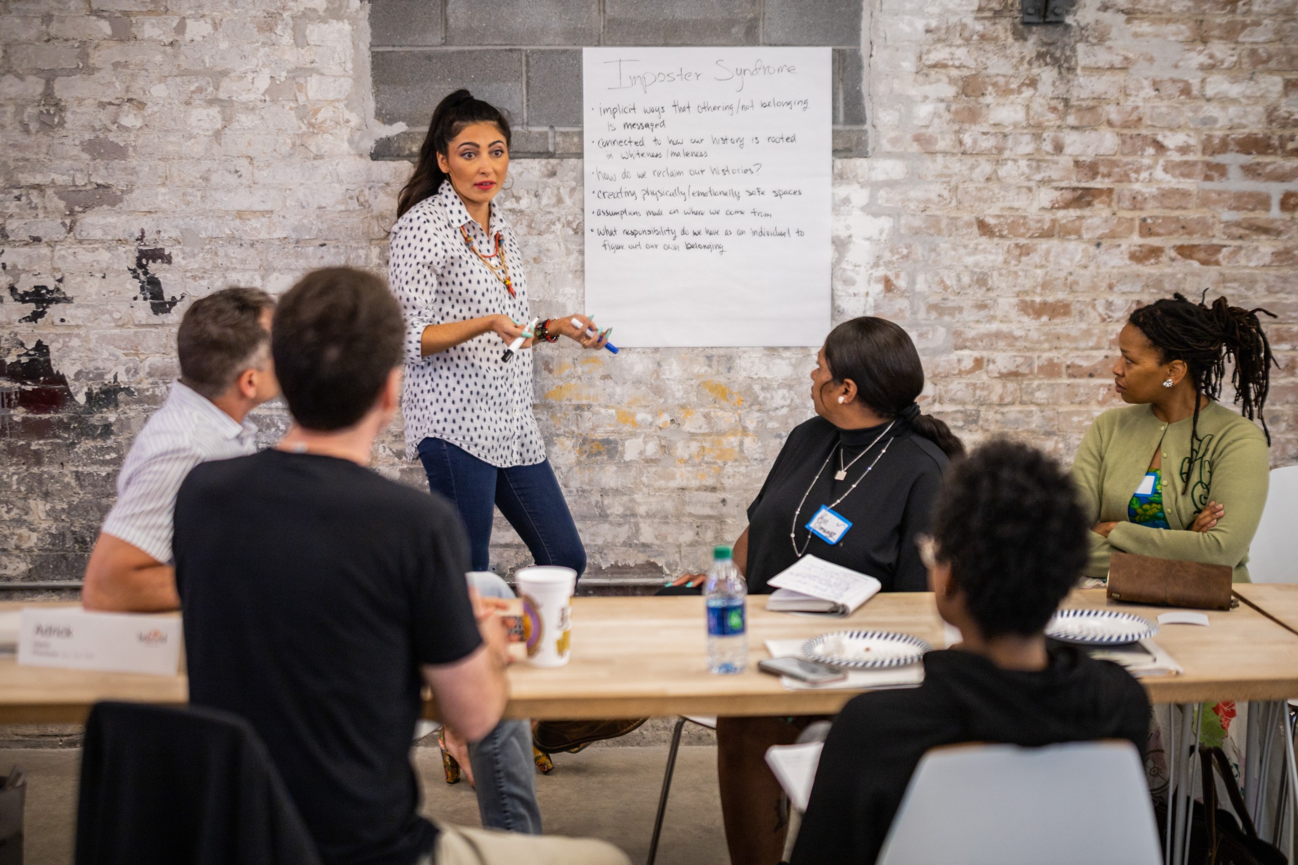 woman speaking with white board behind her in front of a table where five trainees are seated