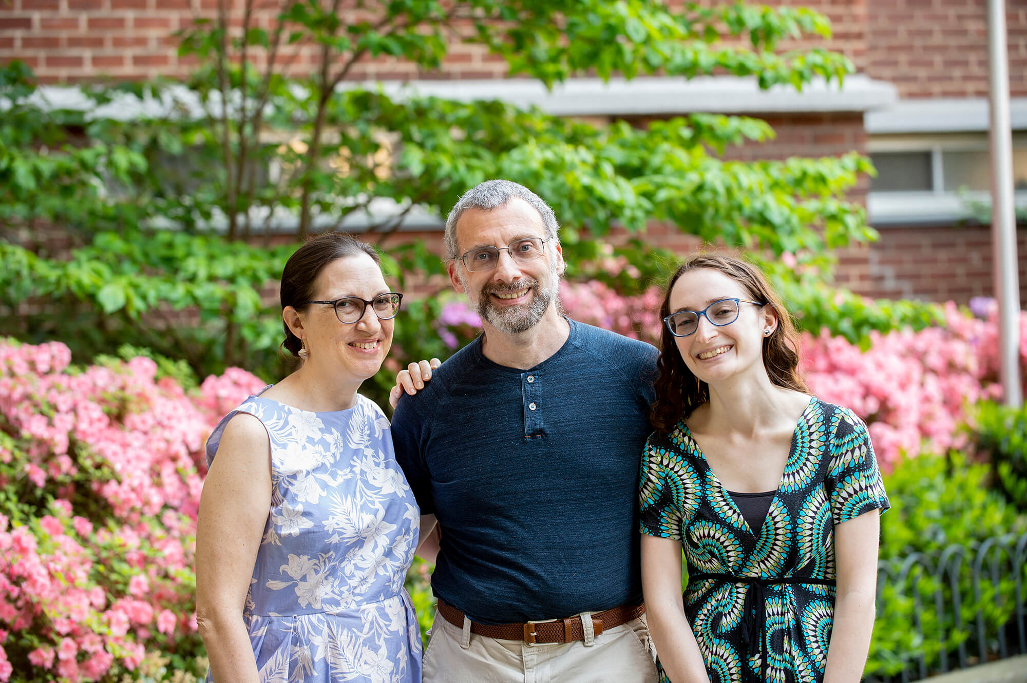 A family of three adults smiles and green foliage is in the background.