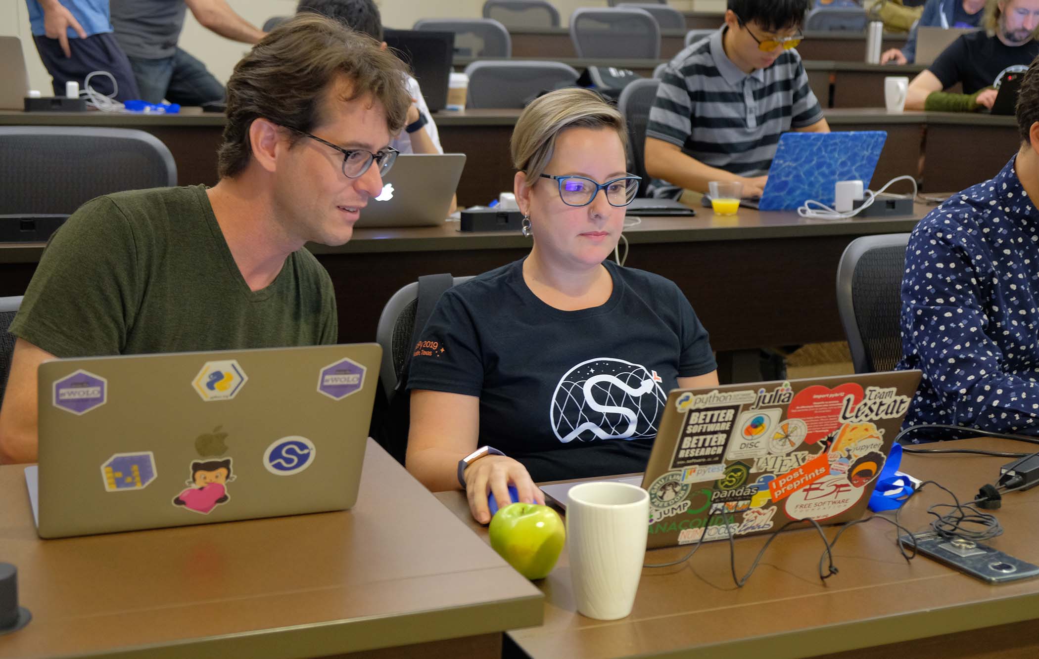 A women and man work on their laptops in a clasroom.