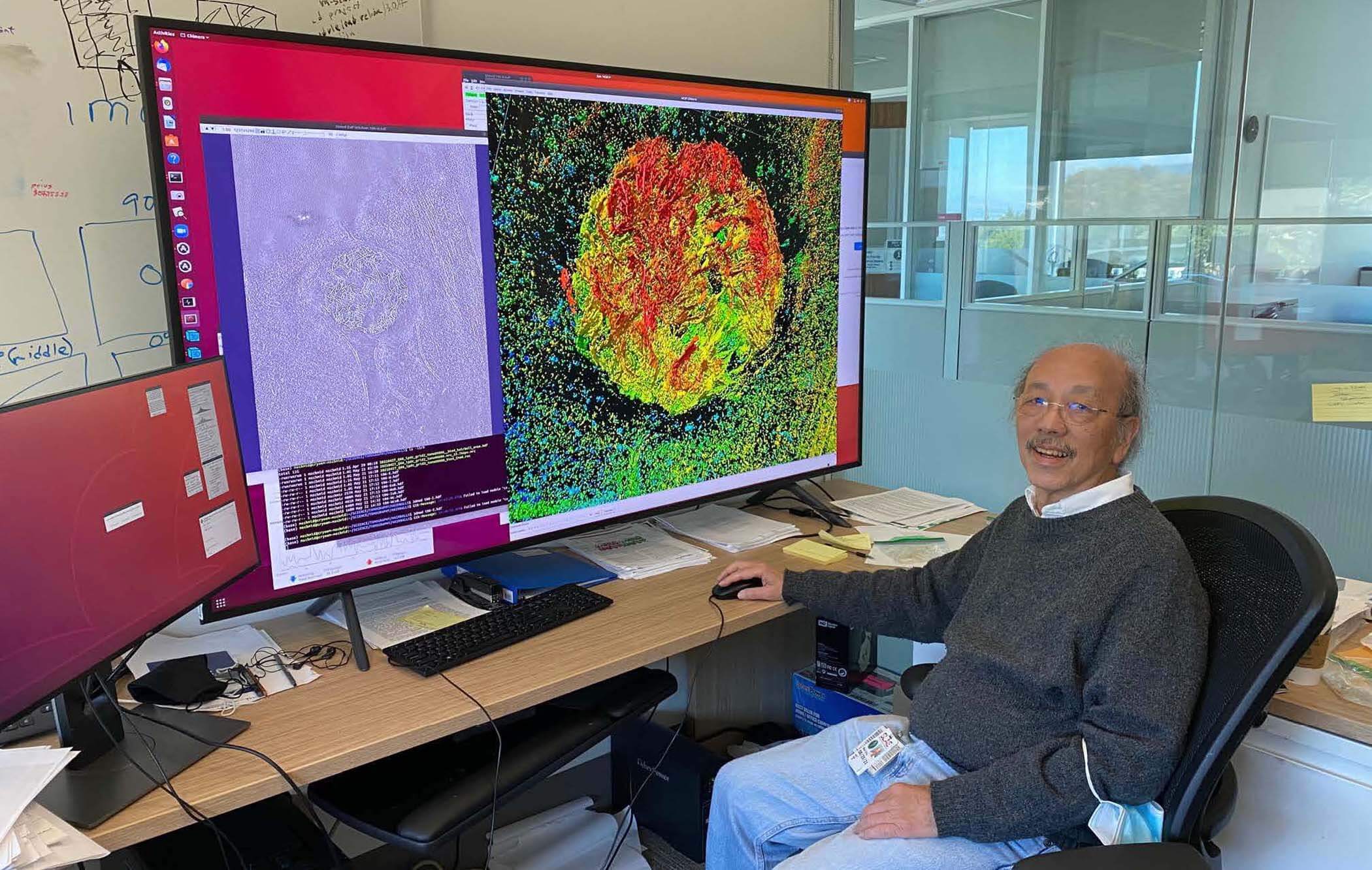 A man sits at a desk with a giant monitor.