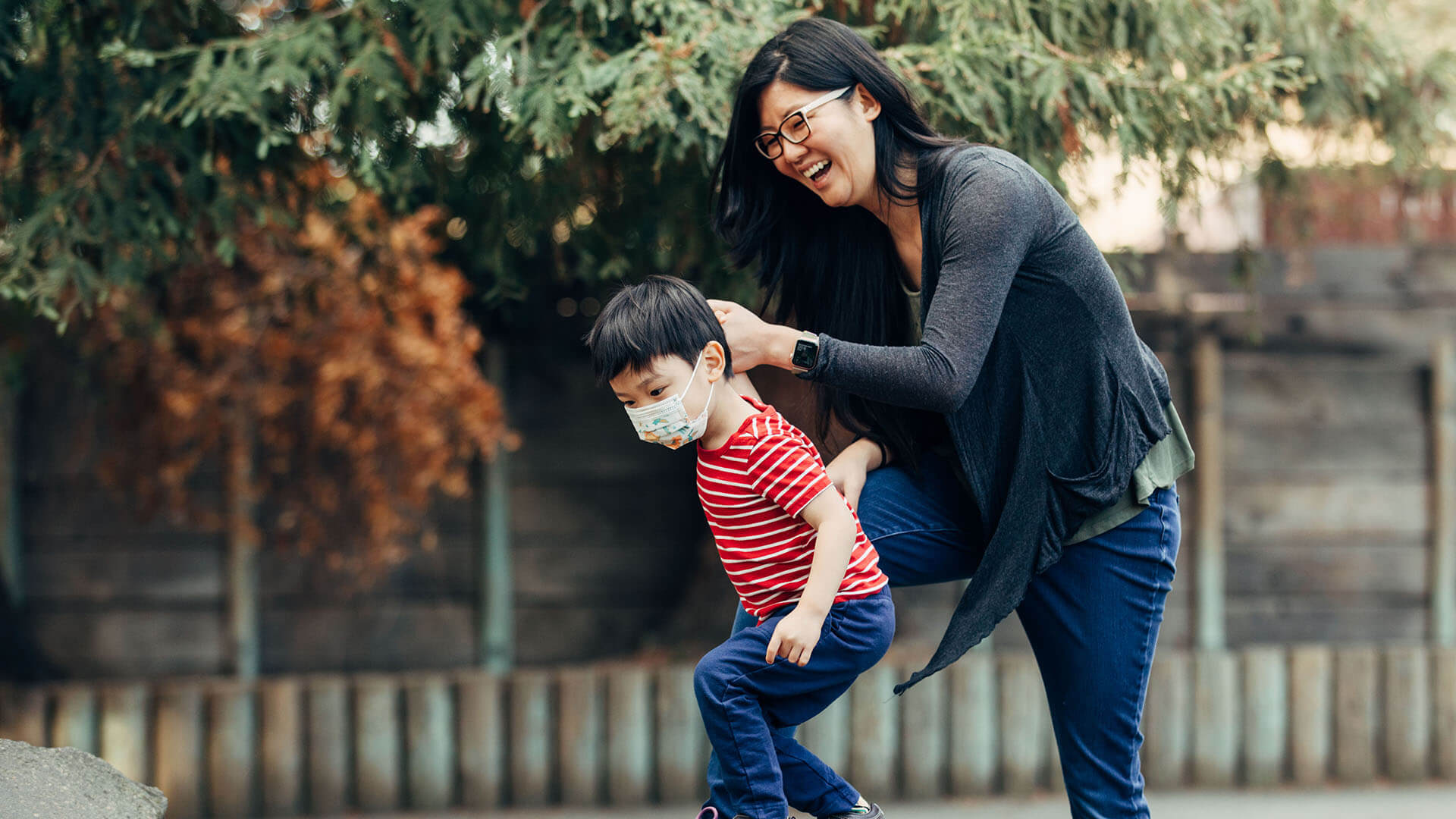 A women smiles while holding the hand of her son who is playing on a playground.