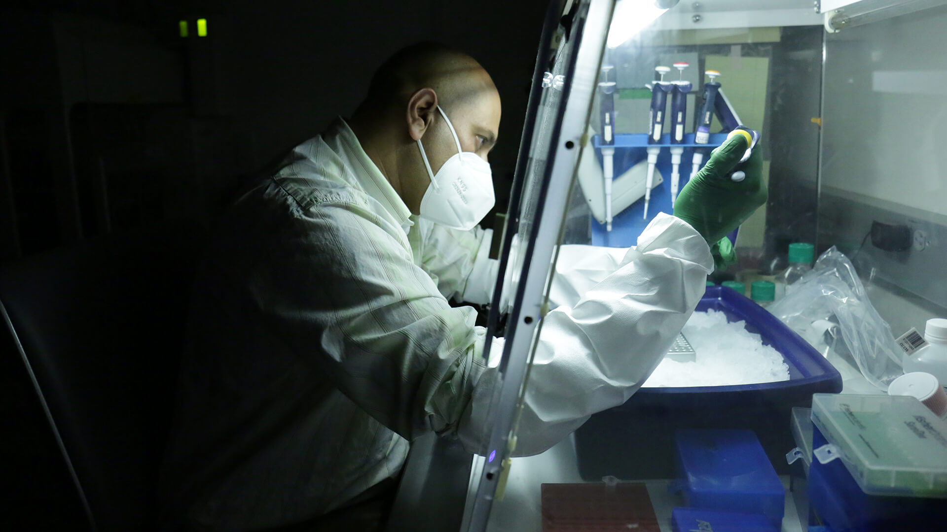 A man in white protective clothing works on a machine in a lab.