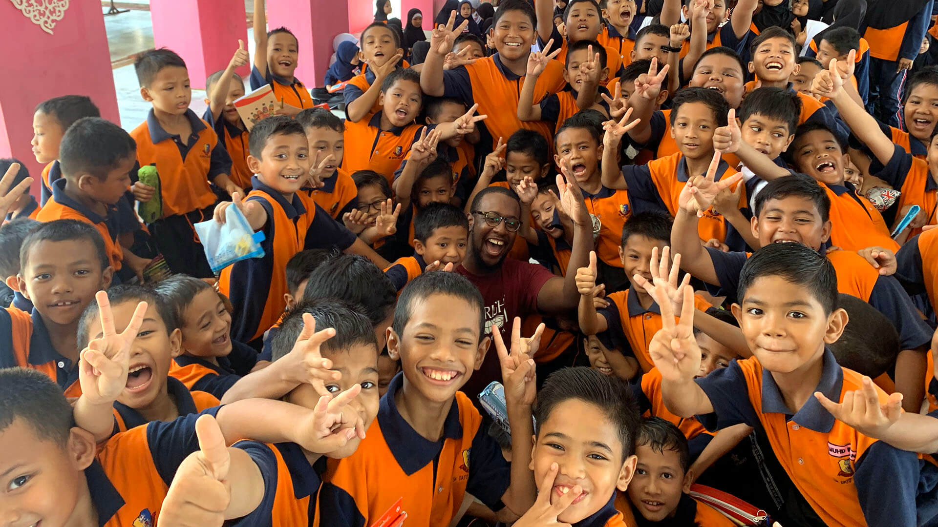 A large group of children smile and wave at the camera.