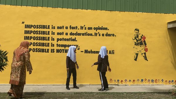 A gif of children putting colorful handprints on a wall that shows a Muhammad Ali quote.