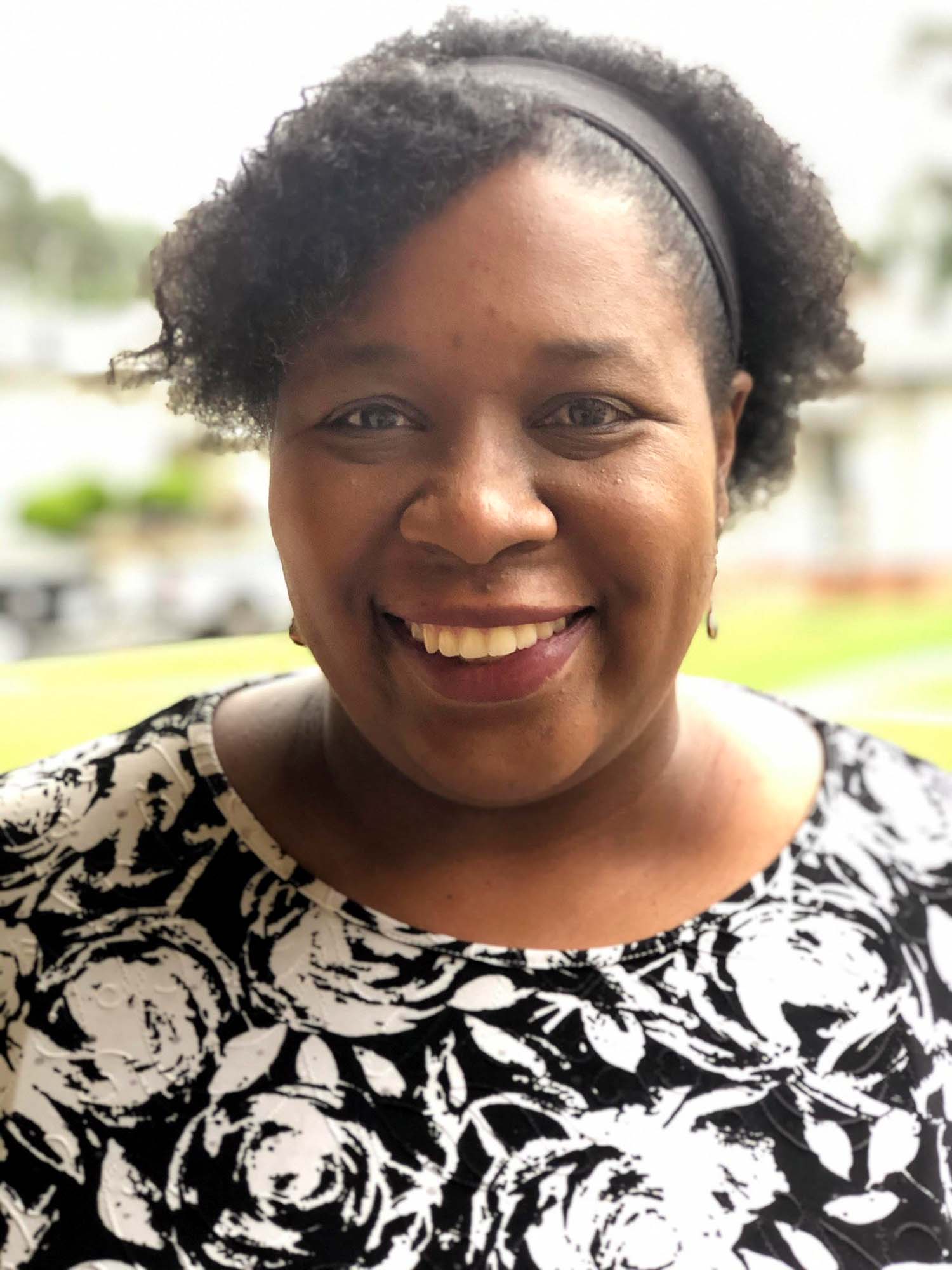 A women wearing a black and white blouse smiles.