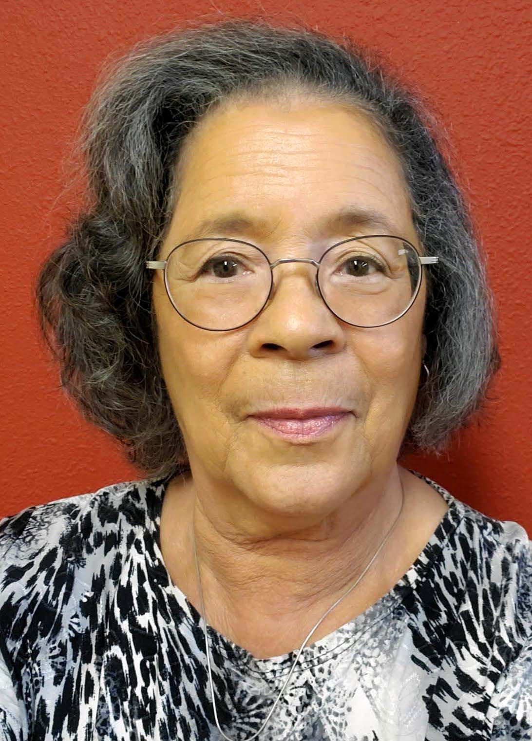 A women with glasses wearing a black and grey blouse.