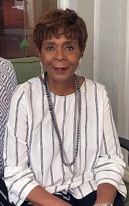 A portrait of a woman in a white blouse, wearing long necklaces.