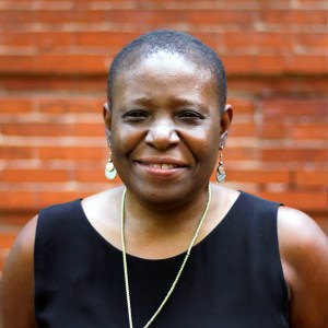 A woman smiles and wears a black blouse and earrings.