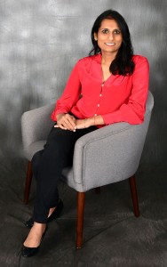 A portrait of a smiling woman wearing a red blouse and sitting in a gray chair.