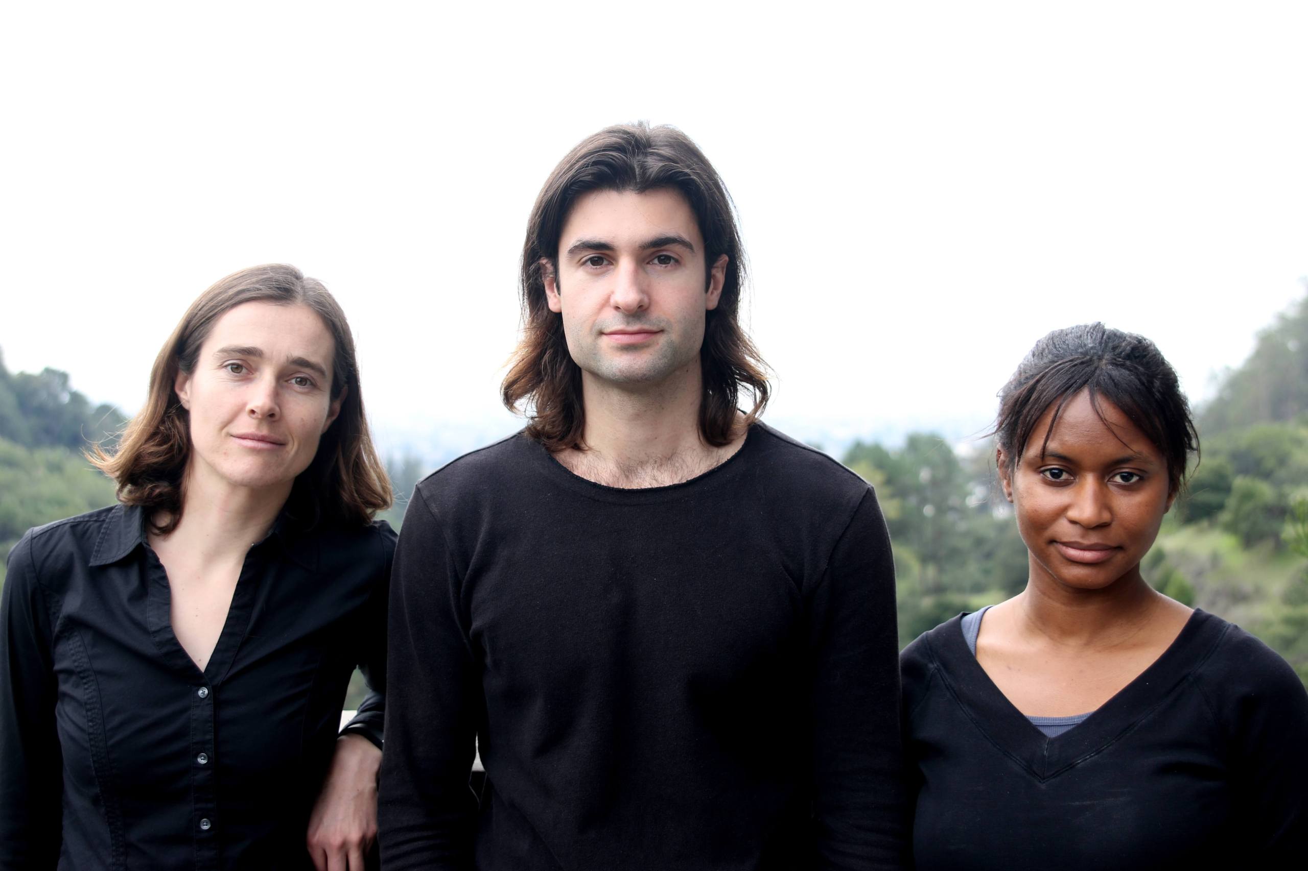 A headshot of three people in black tops with trees and a clear sky in the background. 