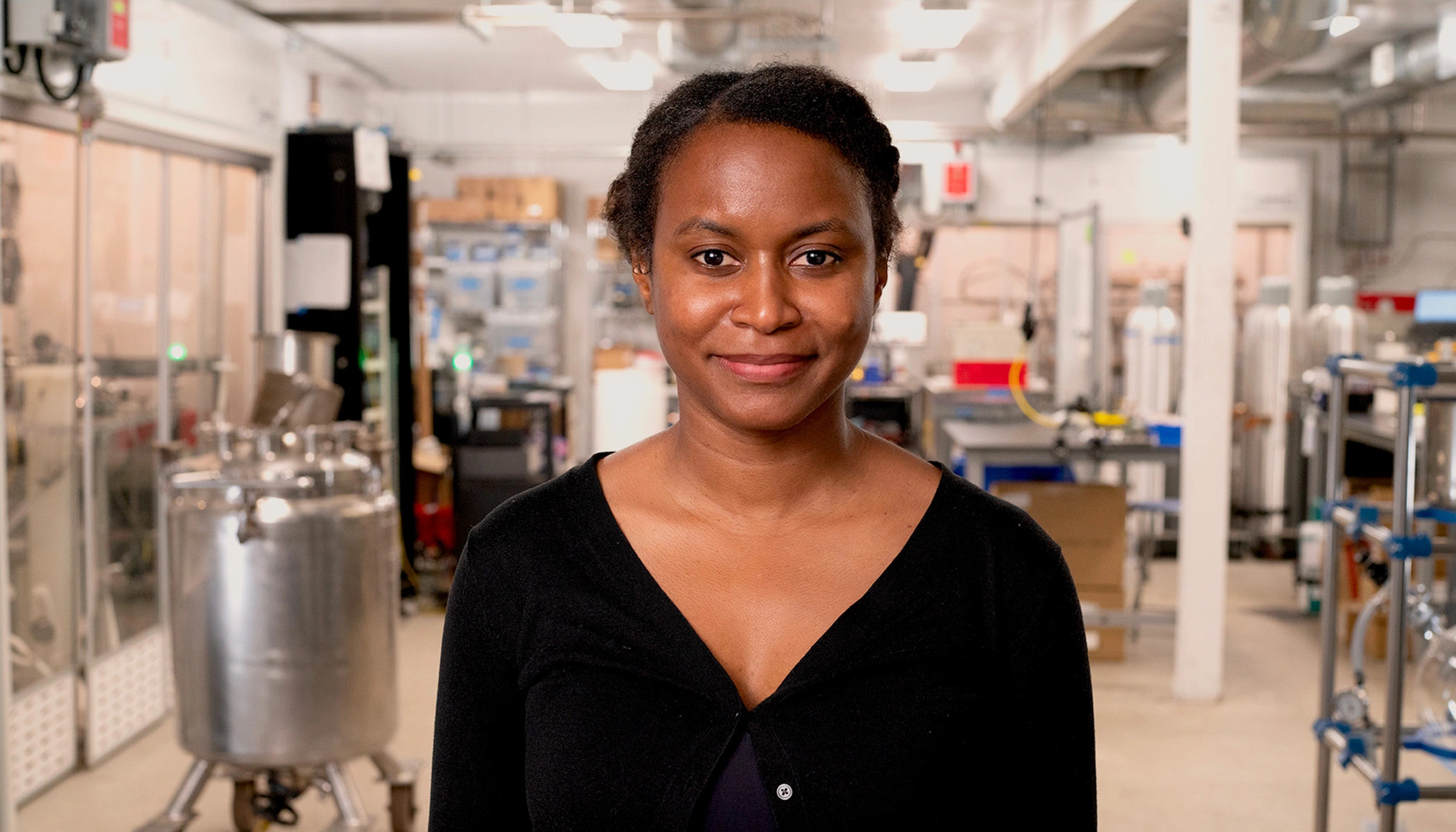 A woman wearing a black top smiles while standing in a lab.