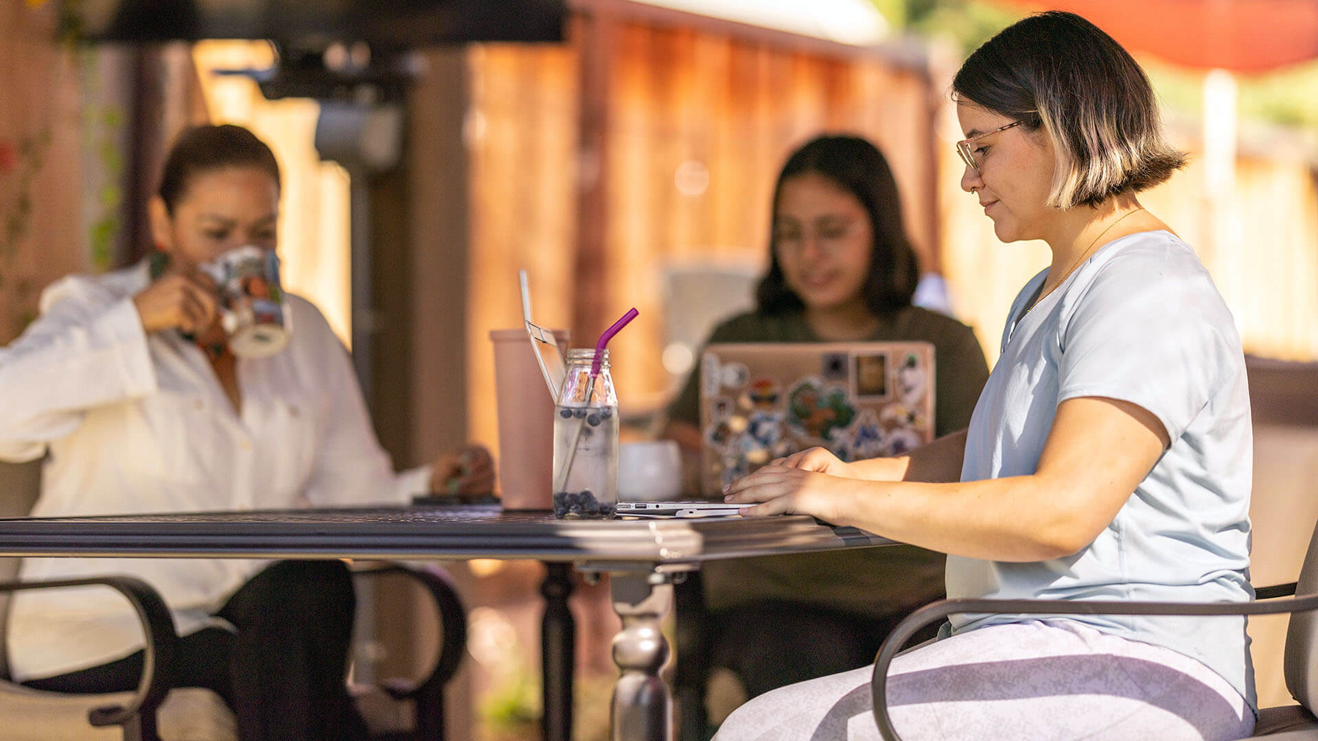 Three women sit outside working and reading.