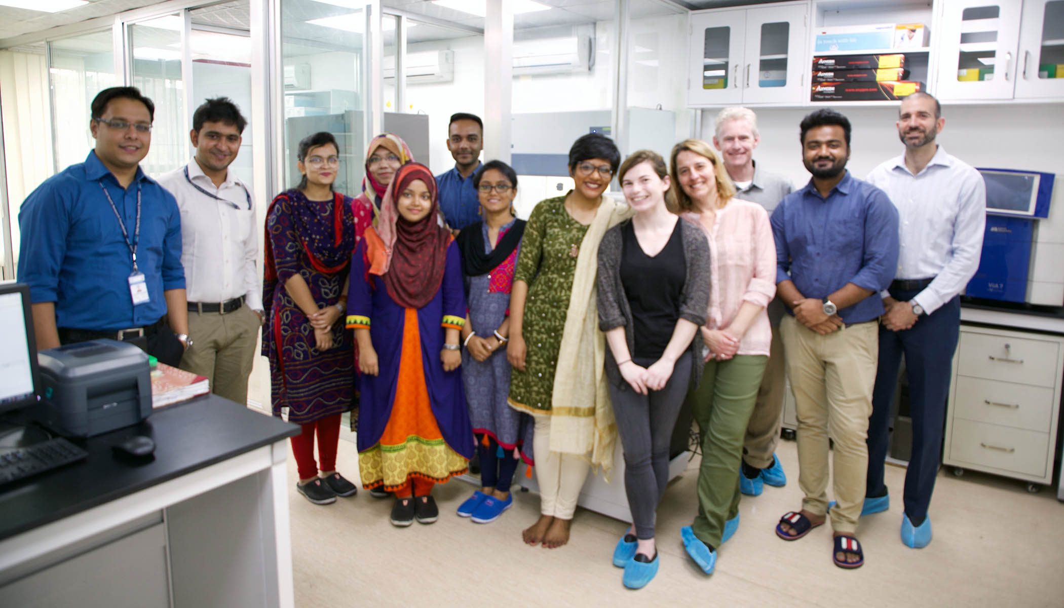 A group of 13 individuals stands together, smiling in a lab.
