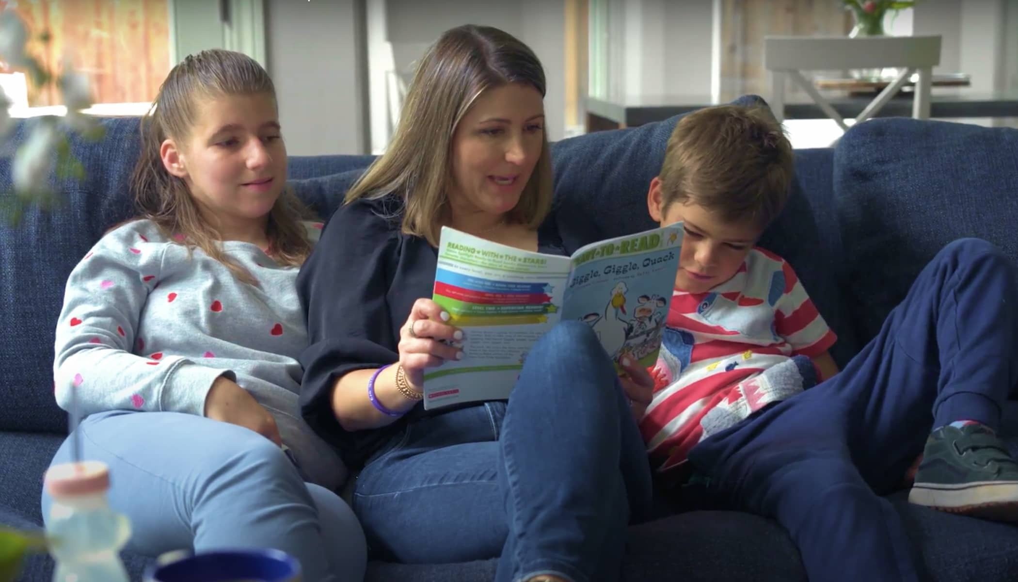 A mother reads to her daughter and son while sitting on the couch.