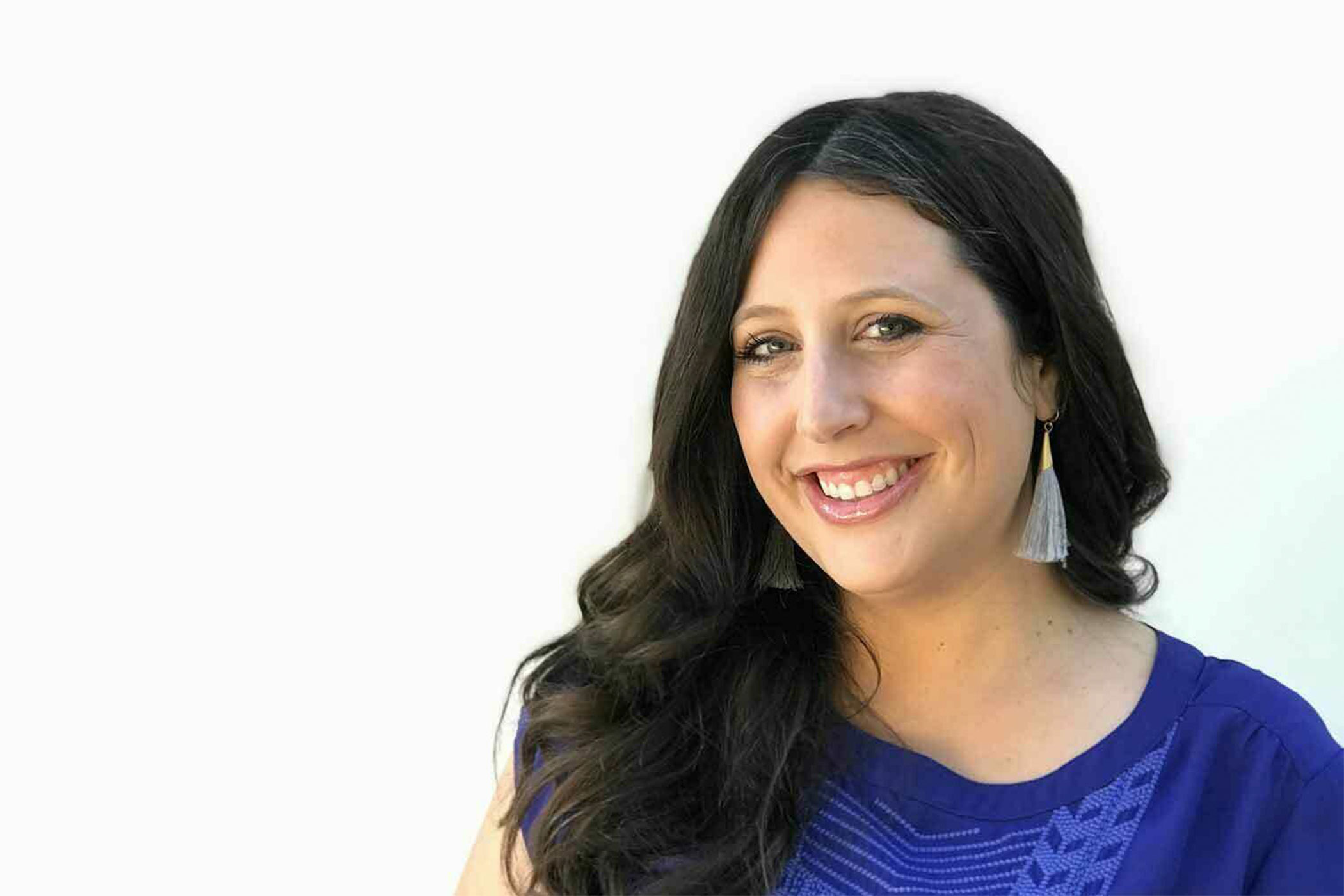 Headshot of Megan Marcus who is smiling and wearing a blue top. She gazes directly at camera. Background is mostly neutral white.