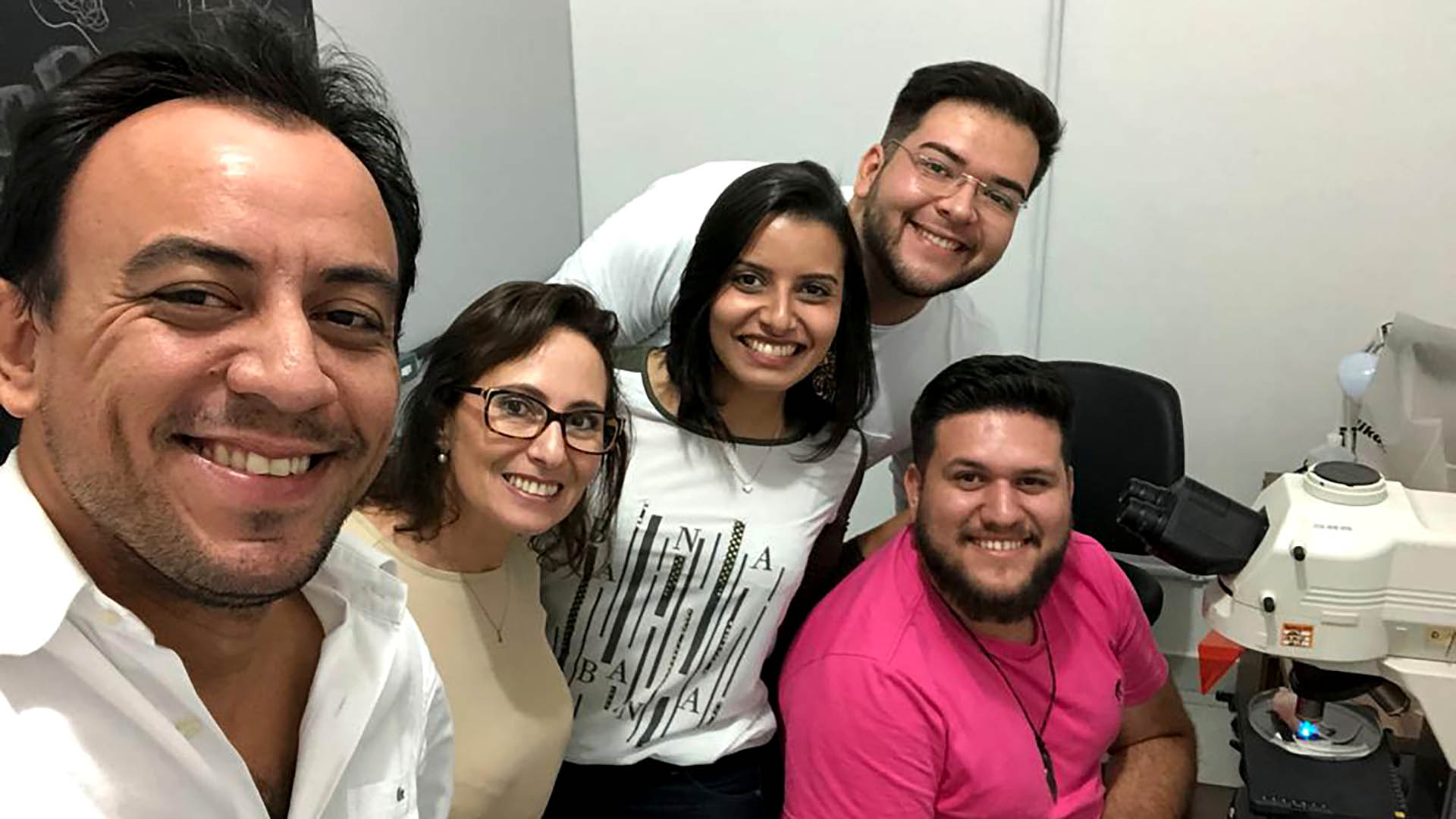A group of people smile for a photo while in a lab. A microscope is visible as well.