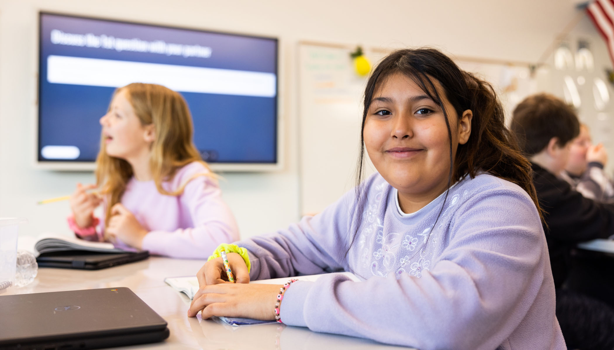 Girl in purple sweater smiles in classroom with other students
