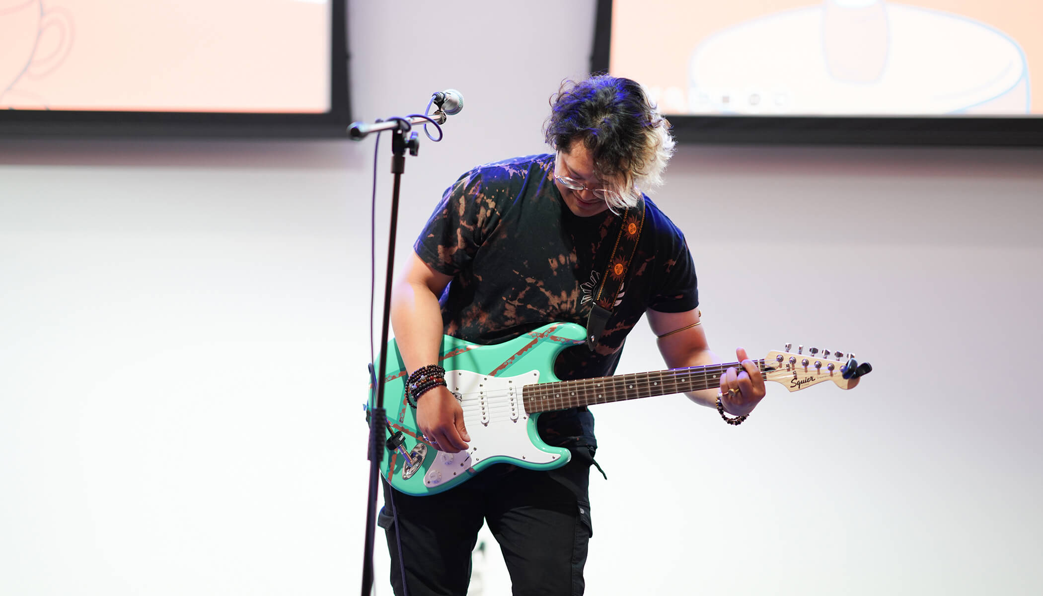 A person looks down at a green electric guitar while playing it in front of a mic.