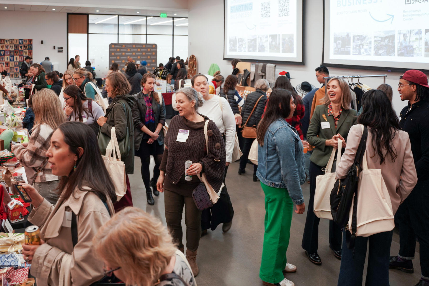 A few dozen people talk and smile in a large event space filled with handmade goods.
