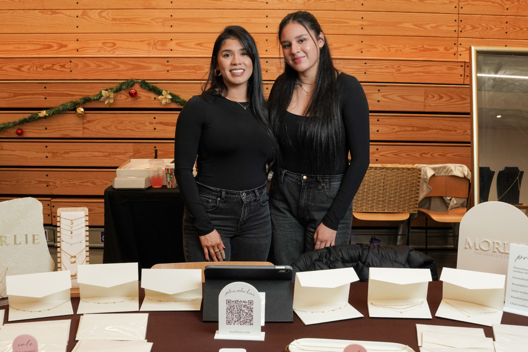 Two women dressed in all black stand behind a table display of greeting cards.