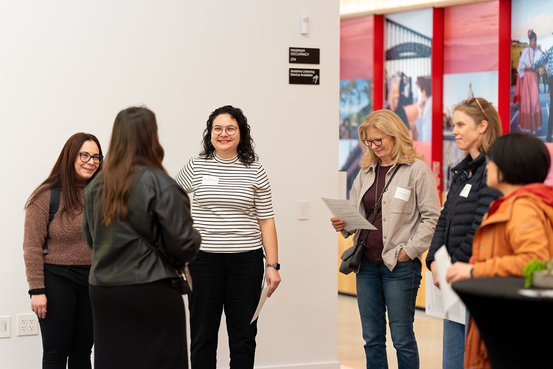 Several people listen and smile as they stand in a small circle.