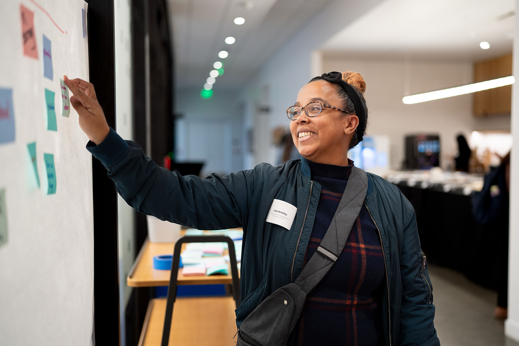 A person puts a teal sticky note on a large white sheet of paper hanging on a glass wall.
