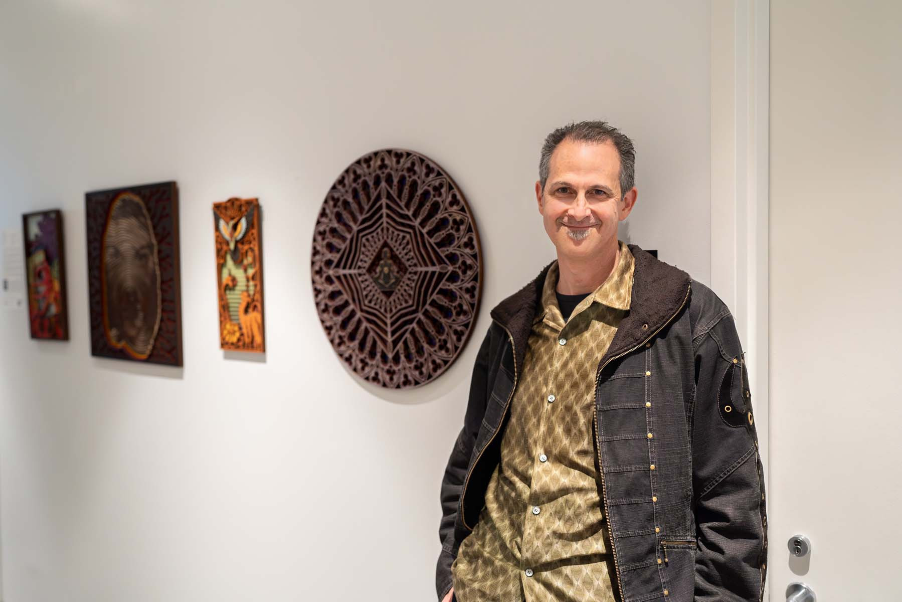 A man leans against a white wall next to three pieces of art.